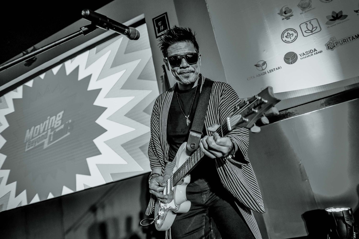 Black and white photo of guitarist performing on stage with dramatic lighting.
