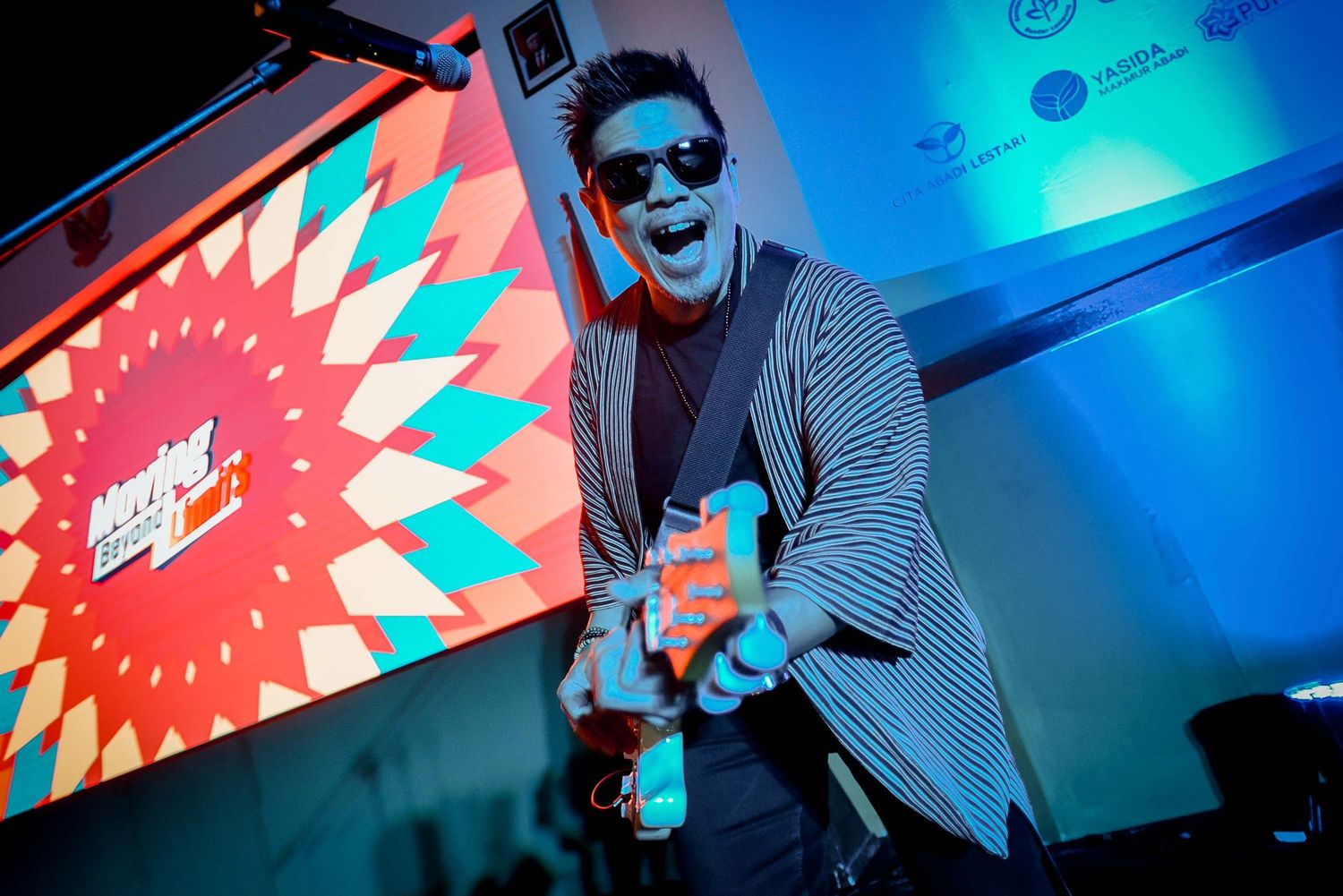Musician performs energetically under blue stage lighting with geometric backdrop design.