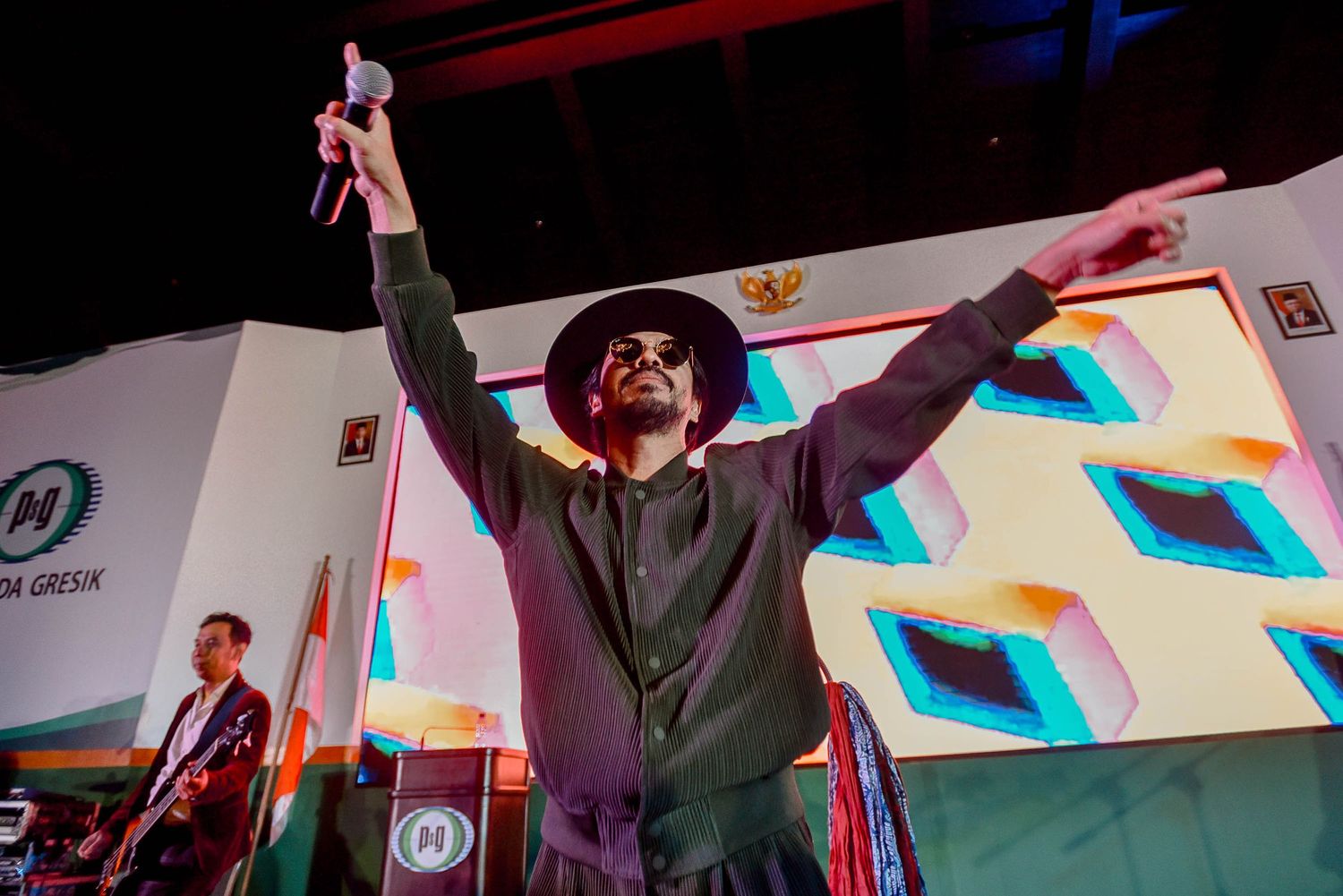 Performer raises arms triumphantly on stage with colorful geometric backdrop.
