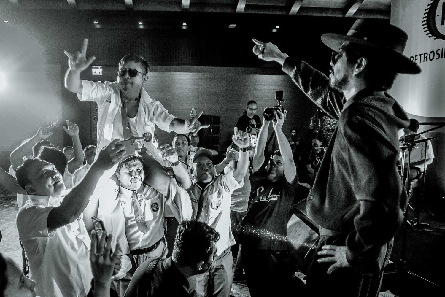 Black and white concert photo showing performers and crowd engaged in lively performance.