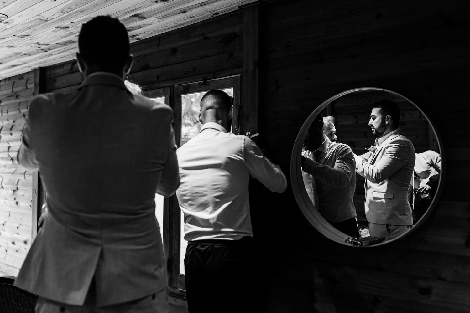 A black and white photo showing figures against a wall with a round mirror reflection capturing a dramatic indoor scene.