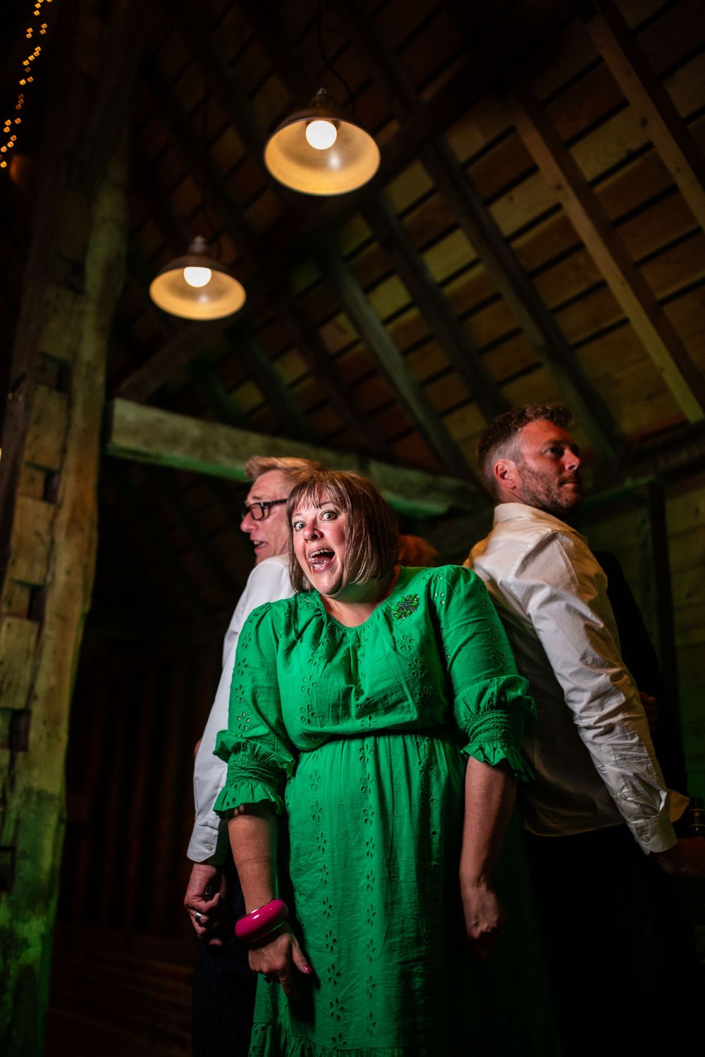 Wedding guests dance and celebrate in a rustic venue with pendant lighting.