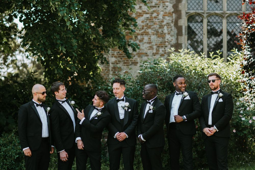 Groomsmen in black tuxedos pose together for a formal wedding photo.