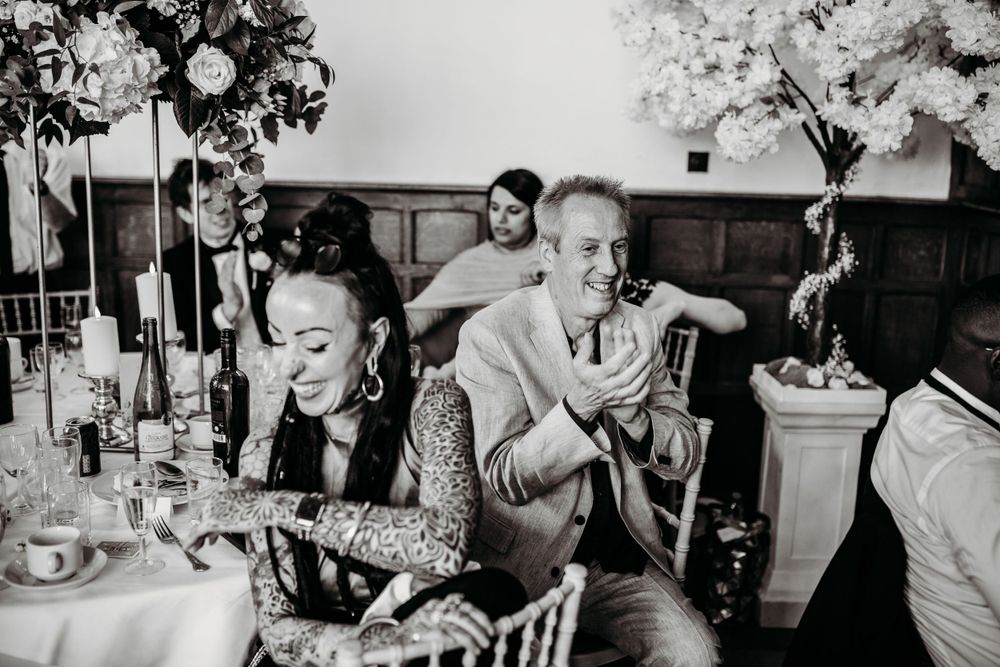 Wedding guests share candid laughter and joy at a dinner reception with candles and floral decor.