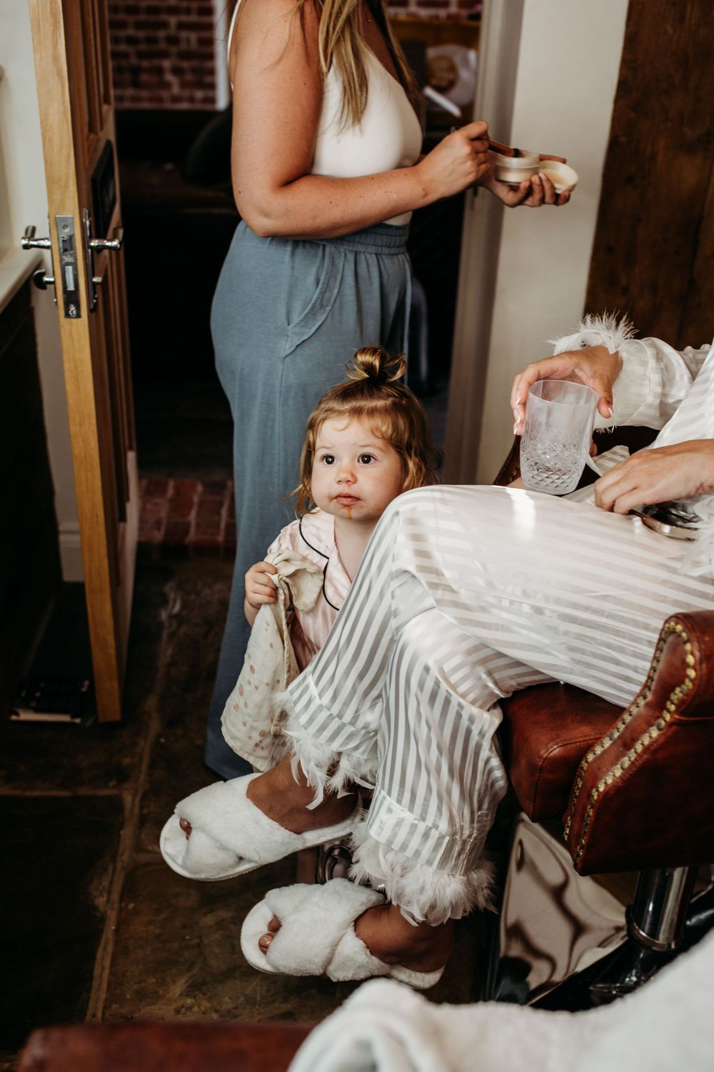 A small child in striped pajamas sits on leather furniture during wedding preparations.