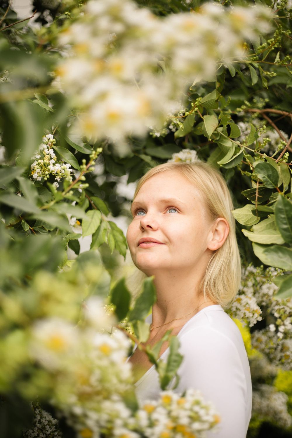 Dreamy upward-gazing portrait surrounded by white spring blossoms and green leaves.