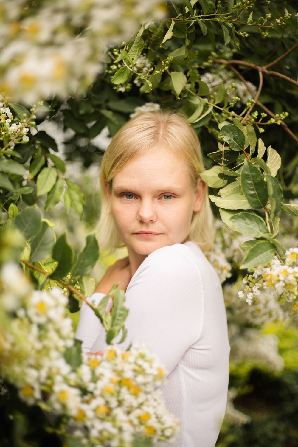 Natural light portrait framed by delicate white flowers and green foliage.