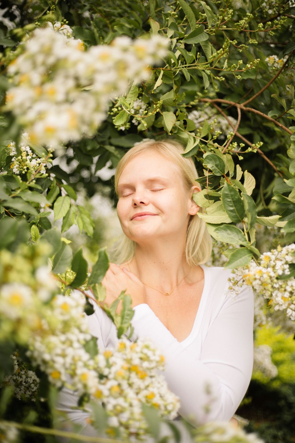 Serene outdoor portrait with closed eyes surrounded by flowering branches.