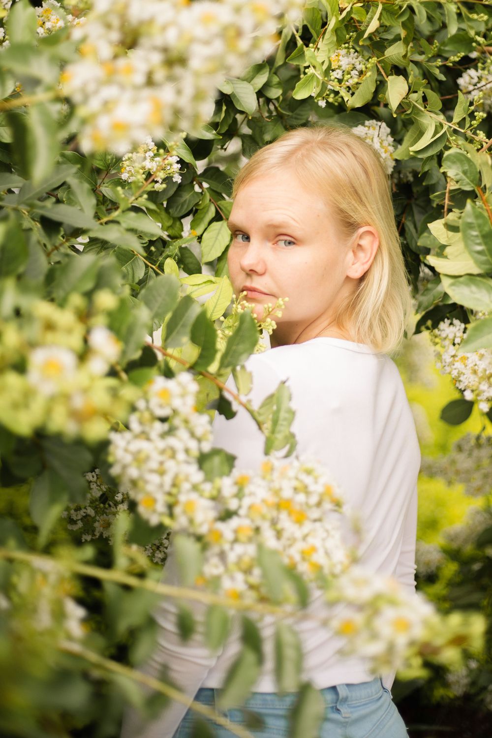 A portrait among flowering white blossoms and green foliage on a sunny day.