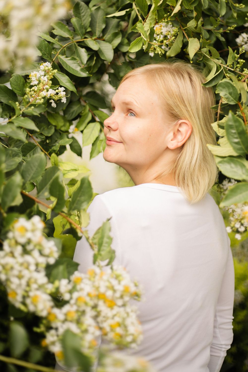 Profile view surrounded by lush greenery and delicate white flowers.