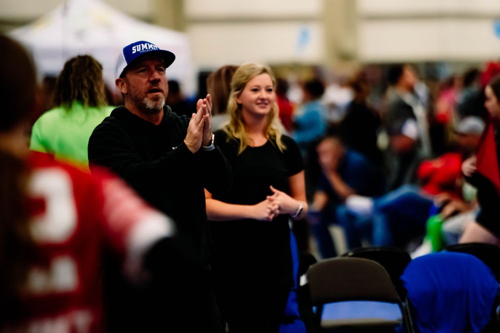 Man and woman clapping and cheering enthusiastically at an indoor volleyball tournament.