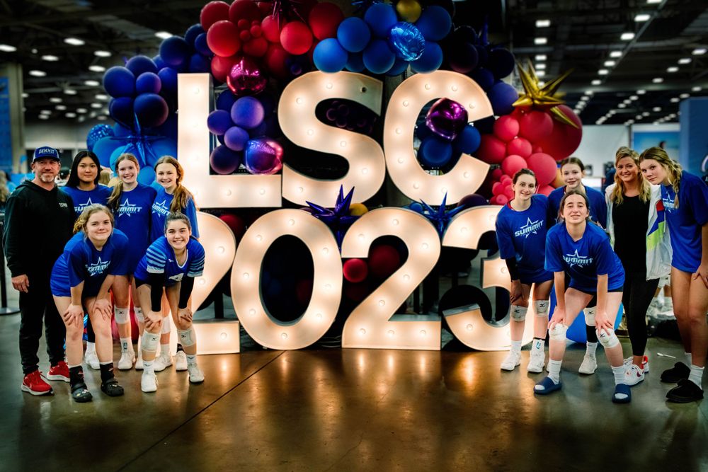 Group of volleyball players posing in front of illuminated LSC 2023 sign with colorful balloon arch.