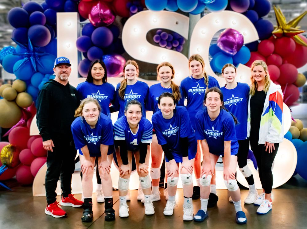 Girls volleyball team in blue Summit uniforms poses in front of LSC balloon display at tournament.