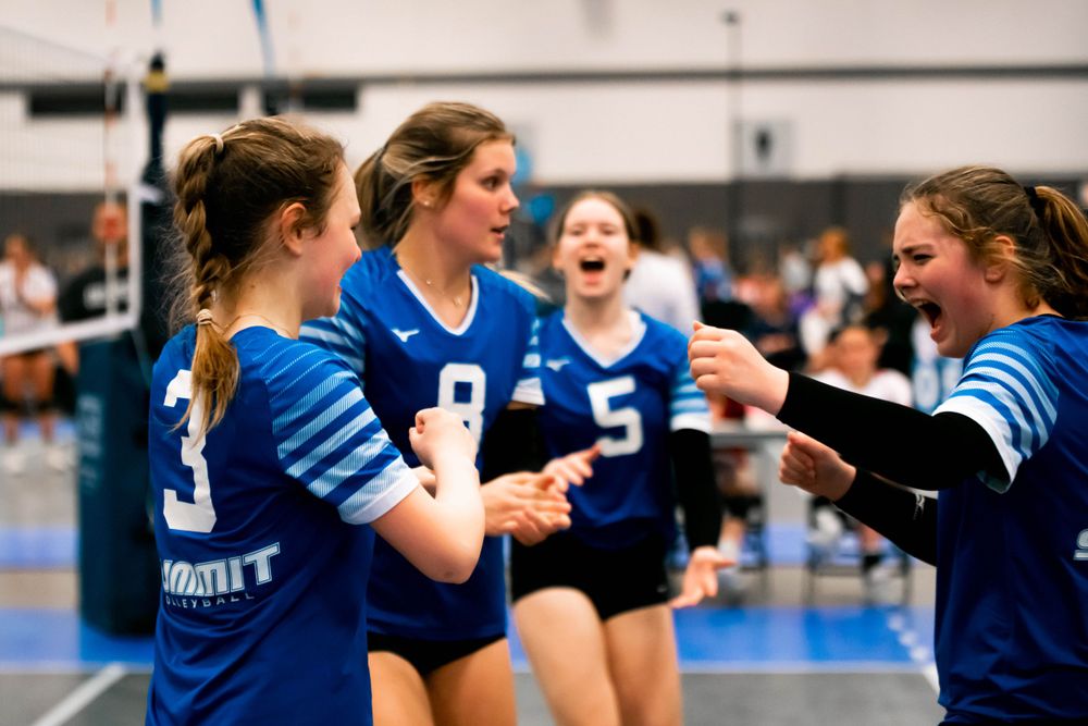 Young female volleyball players in blue uniforms celebrating a point during an indoor match.