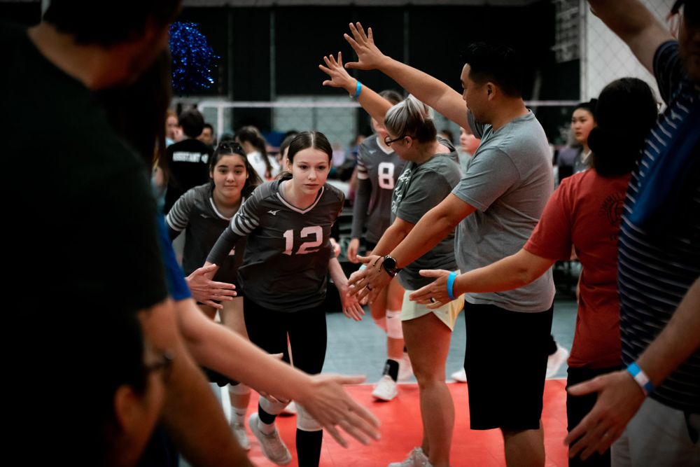 Volleyball player number 12 runs through high-five line during team introductions at indoor tournament.