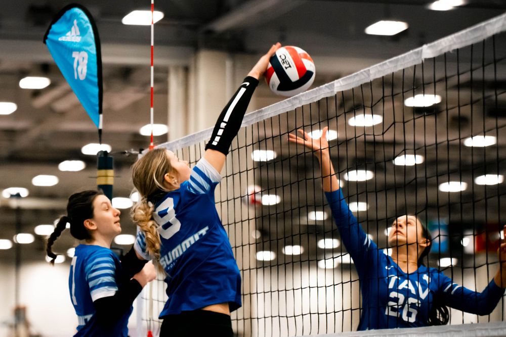 Volleyball players in blue Summit uniforms competing at the net during an indoor tournament.
