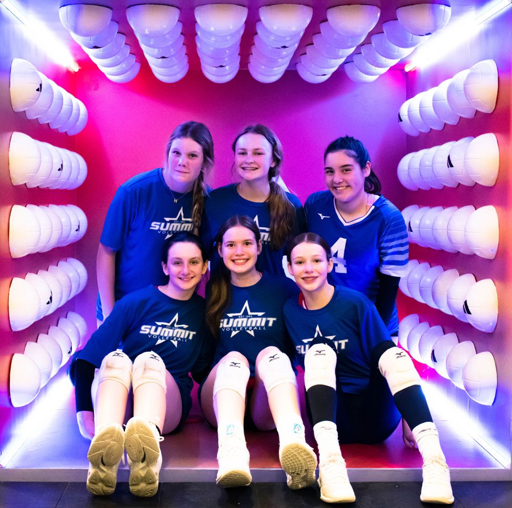 Five young volleyball players posing inside a glowing shoe display booth at a sports event.