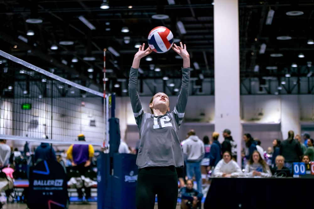 Young female volleyball player in number 12 jersey setting ball during indoor volleyball tournament.