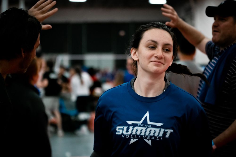 Female athlete in Summit Volleyball blue shirt receives congratulations at indoor volleyball tournament.