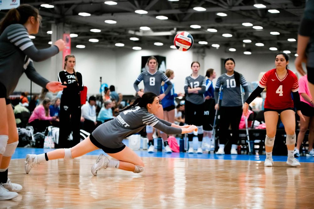 Female volleyball player diving to dig a ball during a competitive indoor volleyball match.