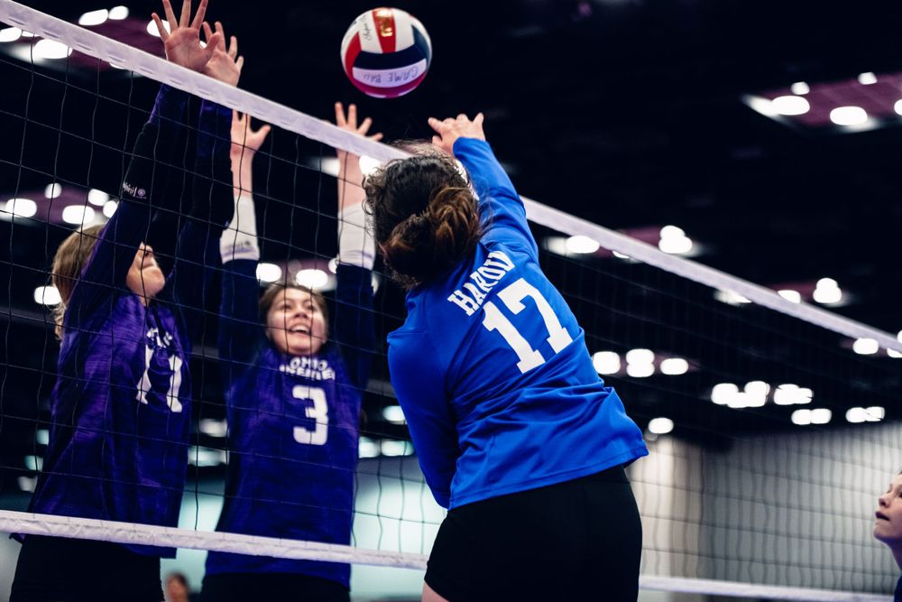 Two players in purple block a spike attempt by blue team player number 17 at the net.