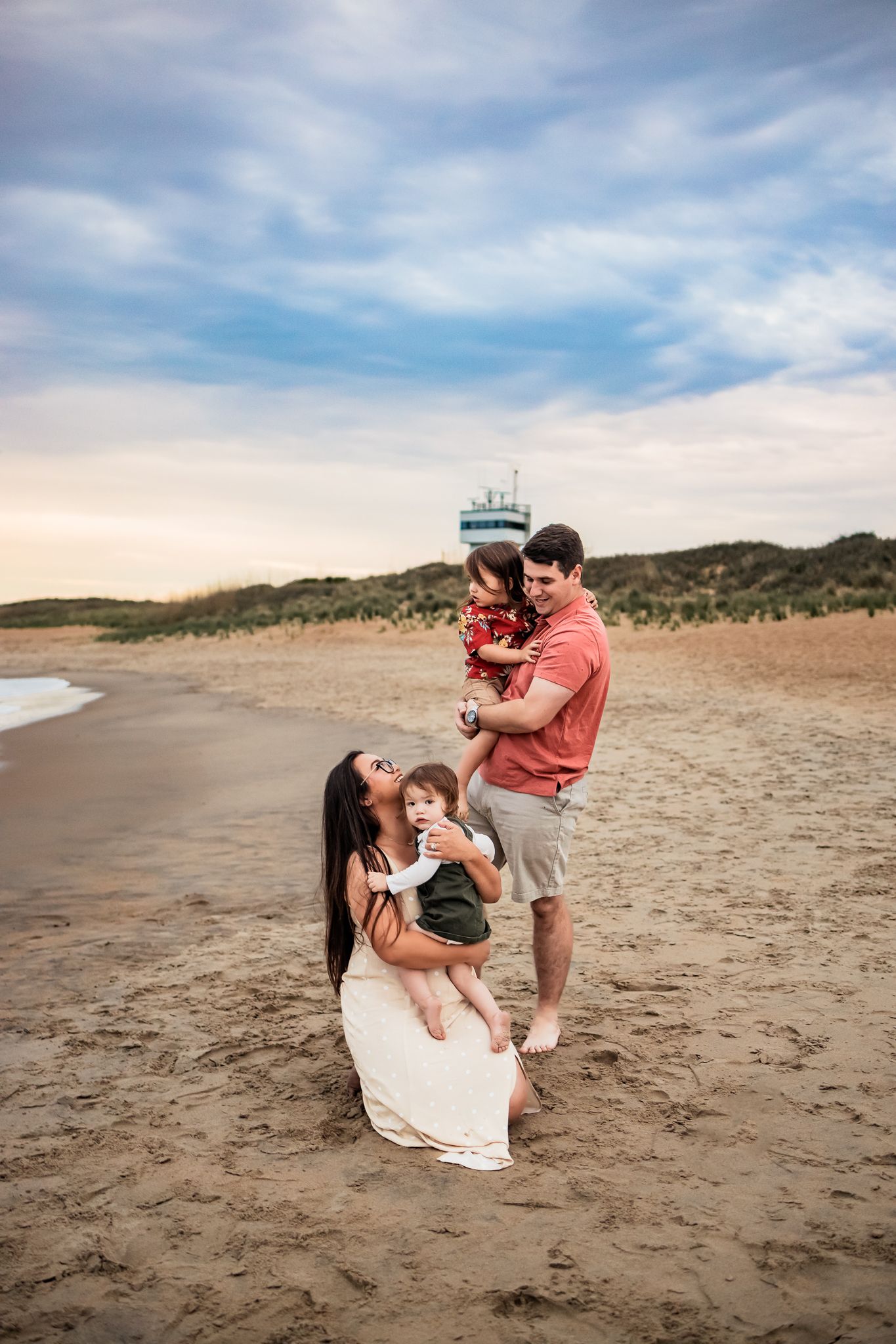 People enjoying a tender moment together on a sandy beach with dunes in the background.