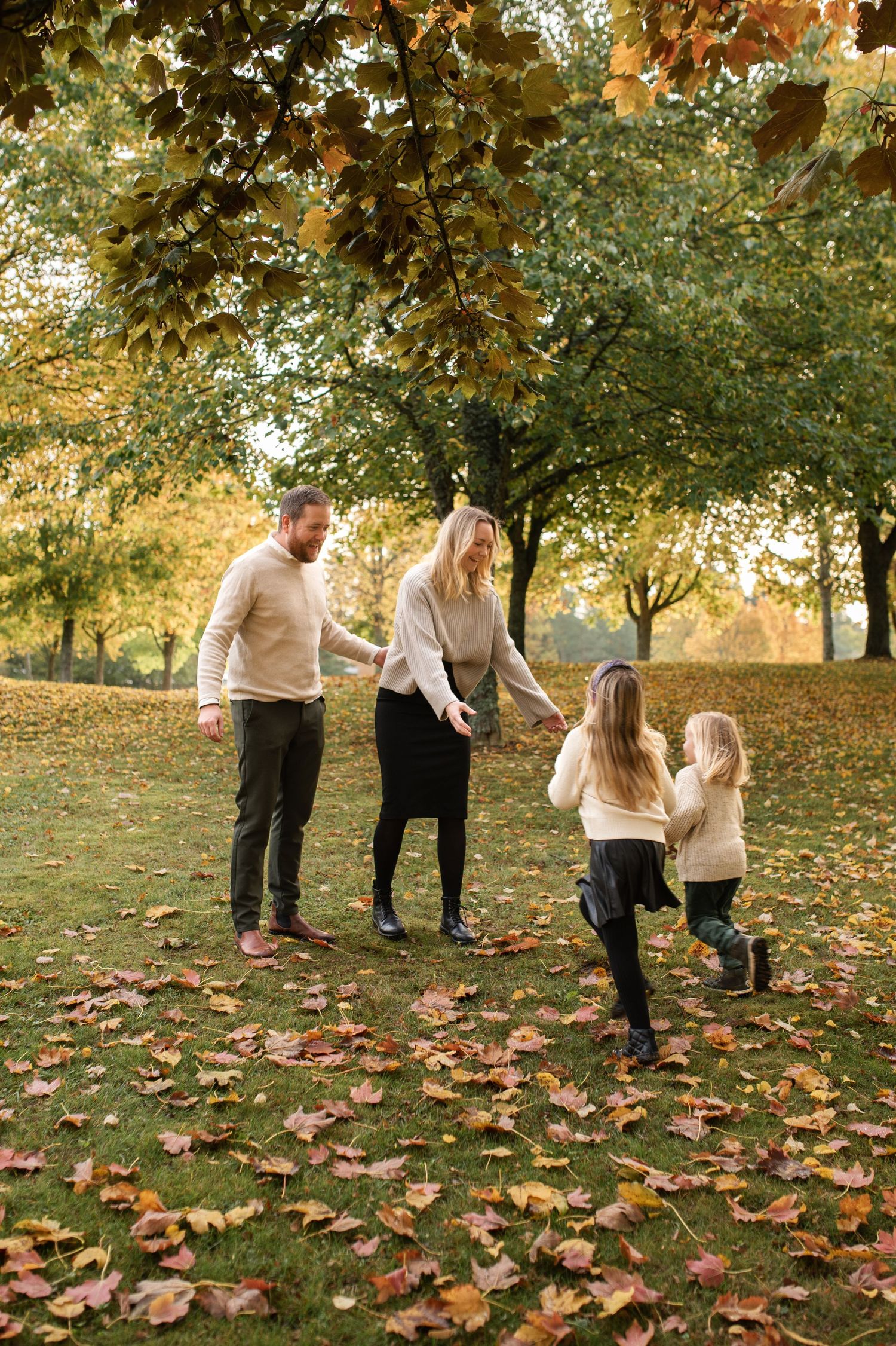 Family enjoying a playful moment together in a park filled with fallen autumn leaves.