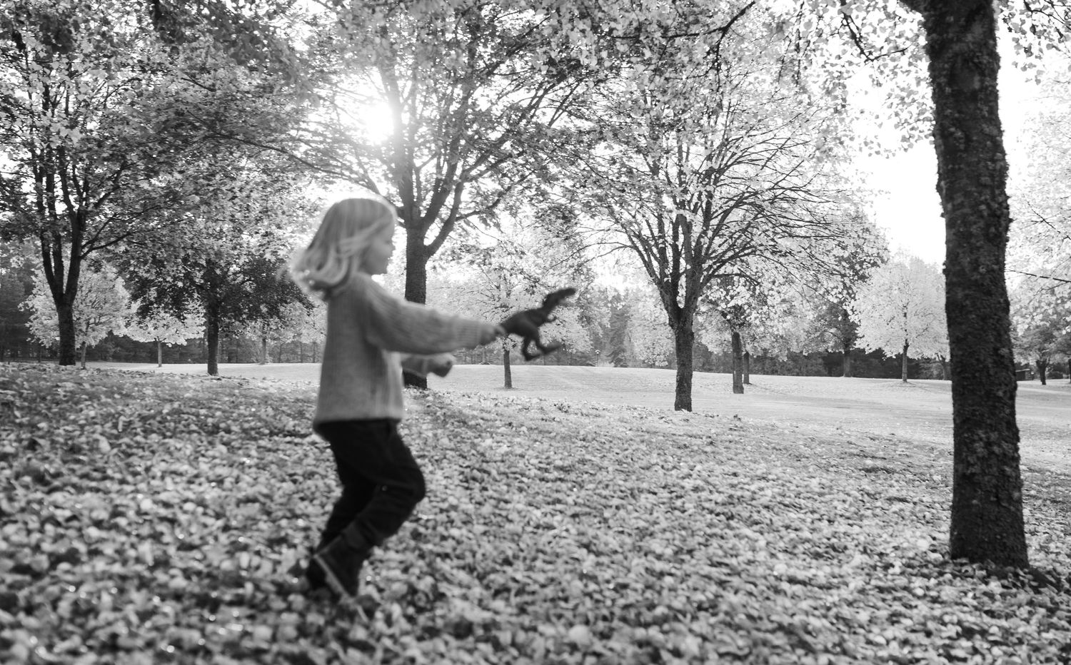 A black and white photo showing movement and joy amidst fallen leaves in a park.