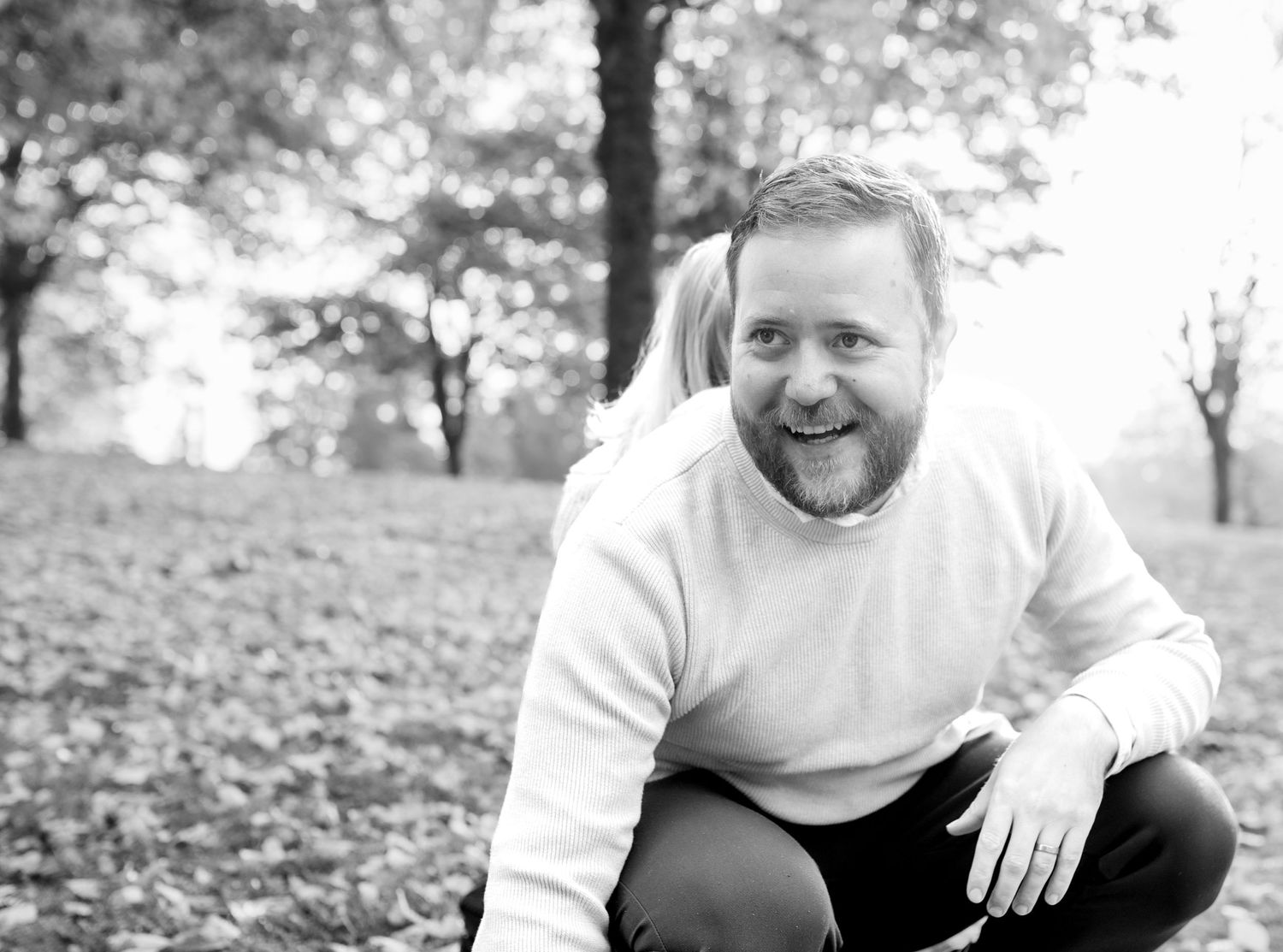 Black and white portrait of a person smiling while sitting outdoors in autumn.