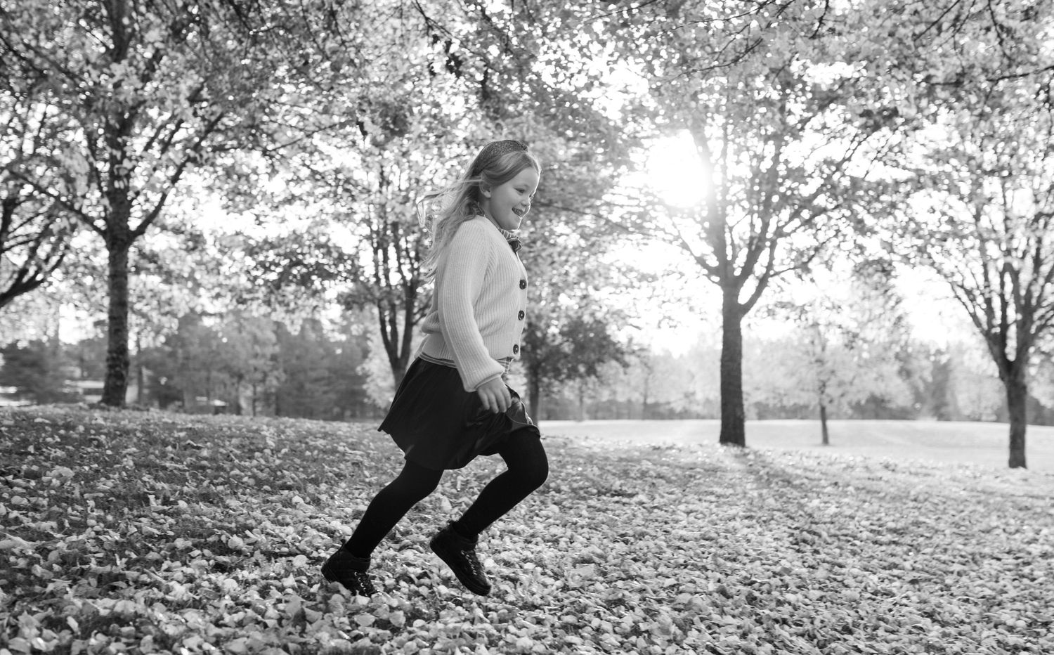 Person in motion captured in black and white among autumn trees with sunlight streaming through.