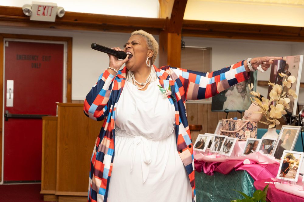 Woman in colorful jacket performing on stage with microphone at a celebration event.