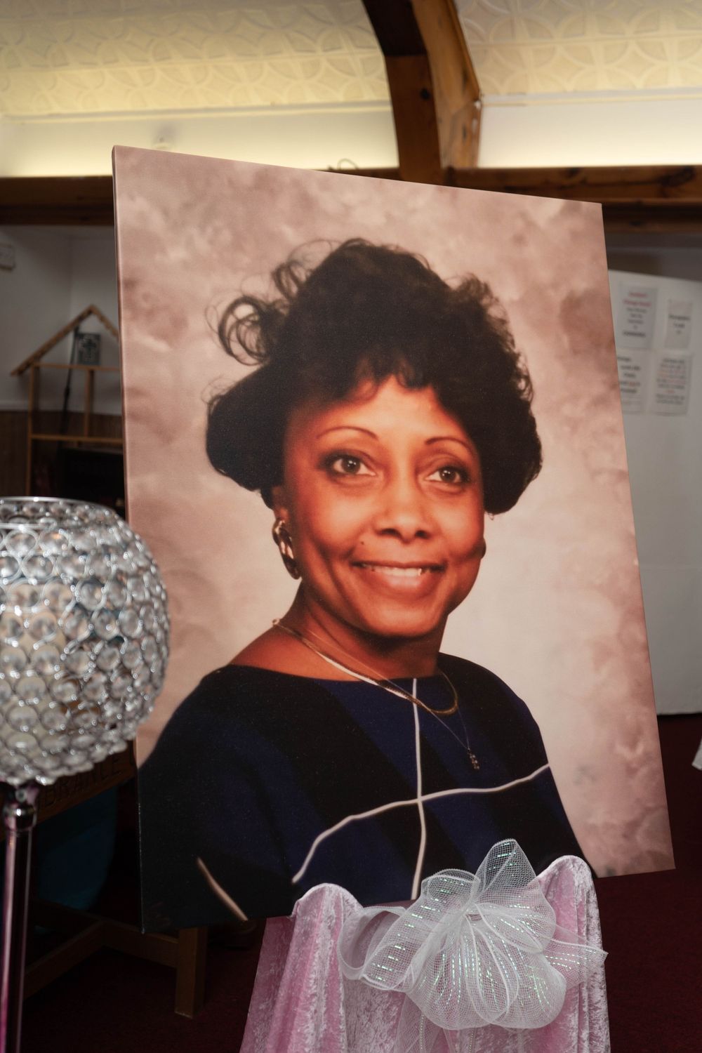 Large portrait photo of a smiling African American woman displayed on an easel with a pink bow at a memorial service.
