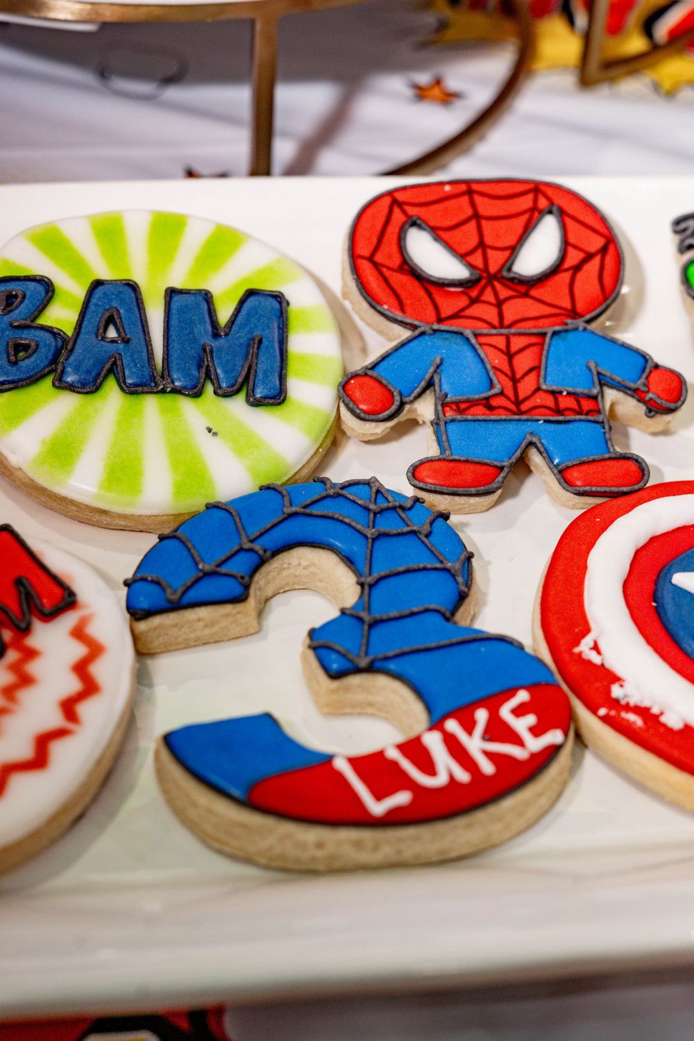 Custom superhero-themed decorated sugar cookies for a third birthday party.