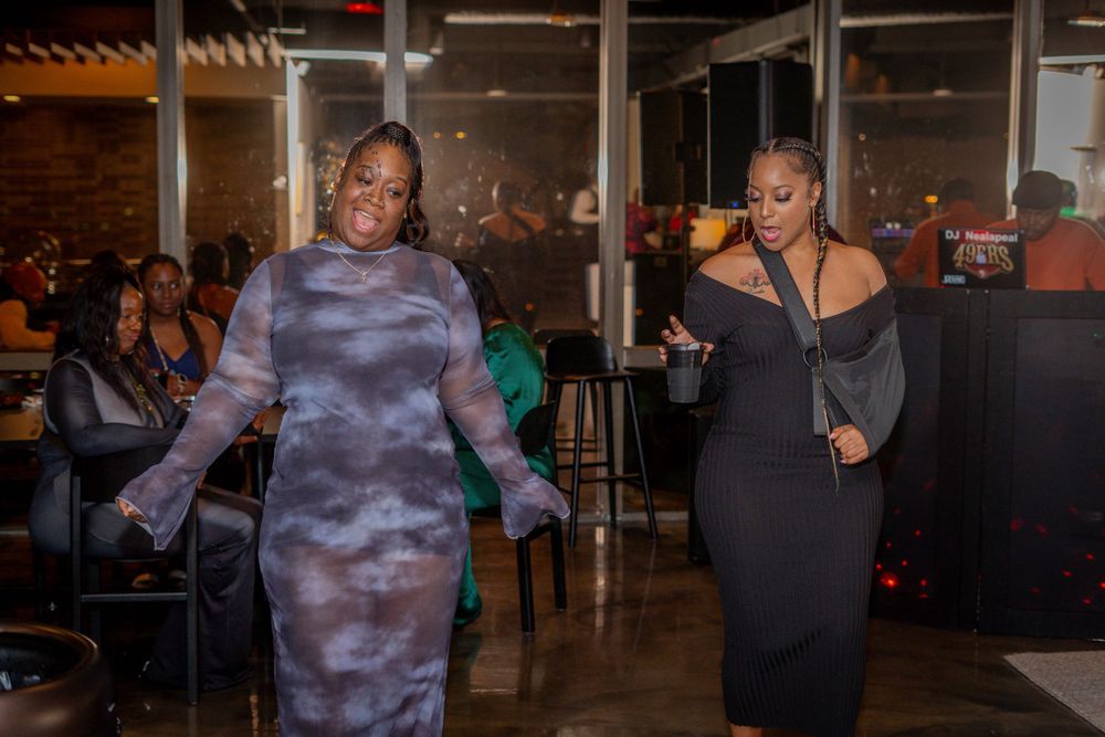Two women in elegant dresses walking through a dimly lit event venue.