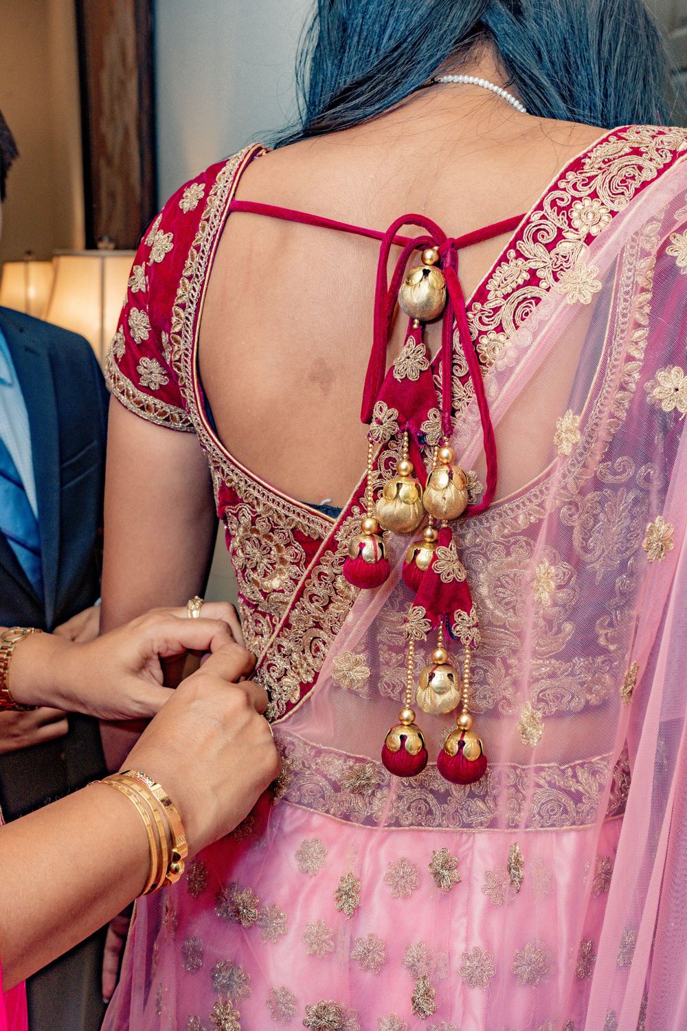 Close-up of ornate red and gold Indian bridal blouse with decorative gold bell tassels.