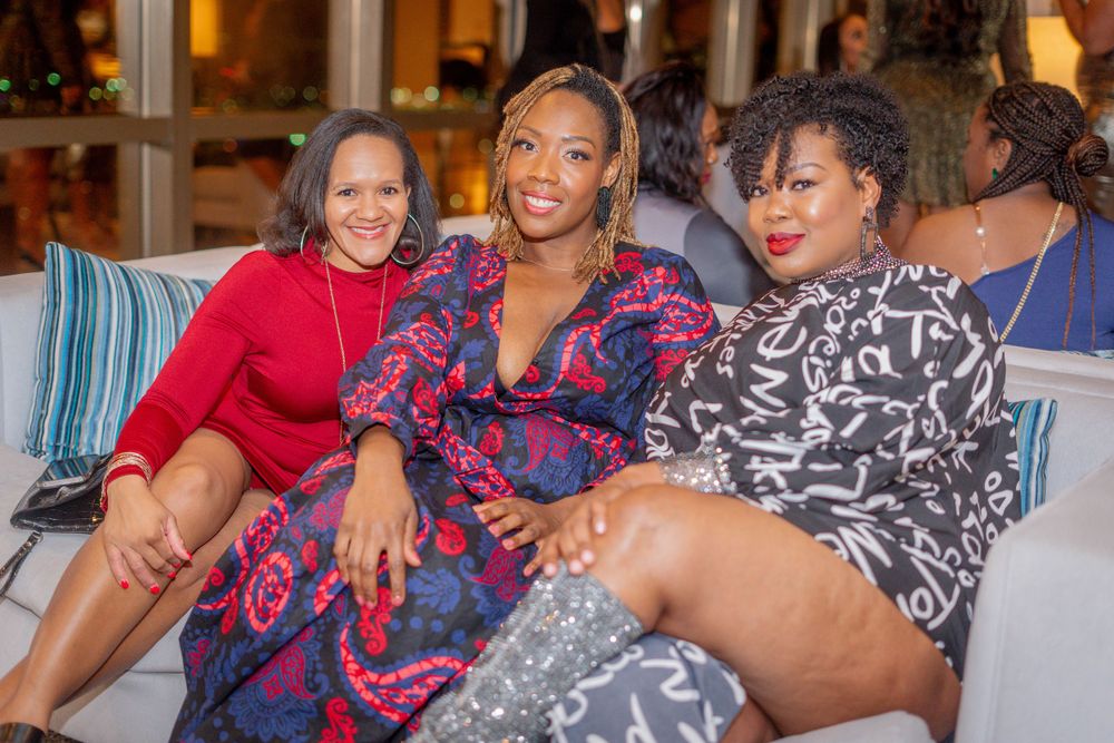 Three women sitting together smiling at an evening social gathering.