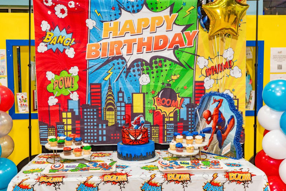 Superhero-themed birthday party decoration with Spiderman backdrop and dessert table.