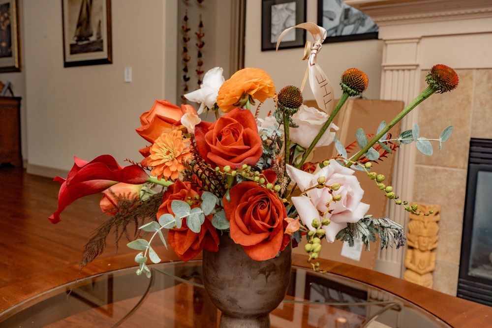 Vibrant autumn floral arrangement with orange roses and red calla lilies centerpiece.