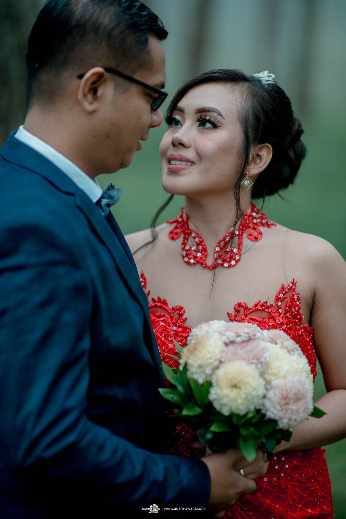 Romantic couple poses with floral bouquet, featuring red formal dress and navy suit.