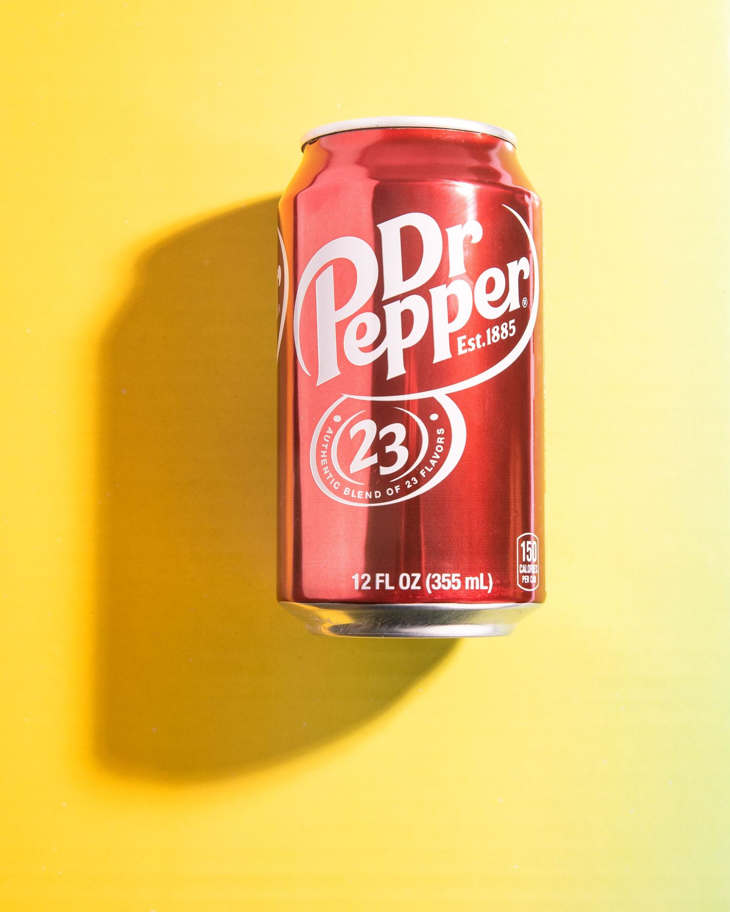 A red can of Dr Pepper soda on a bright yellow background casting a dramatic shadow.