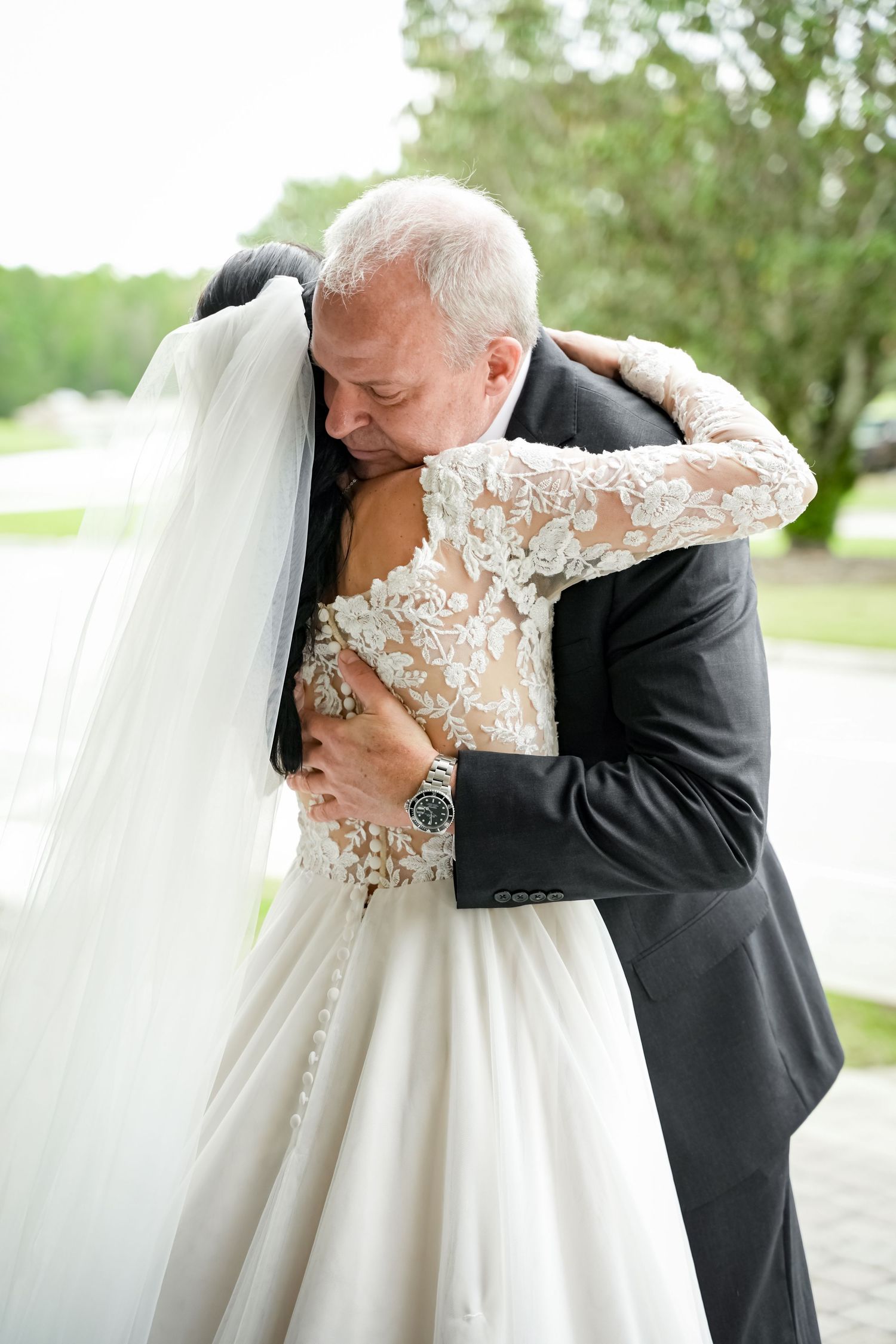 Emotional embrace between father and bride in lace wedding dress during special moment.