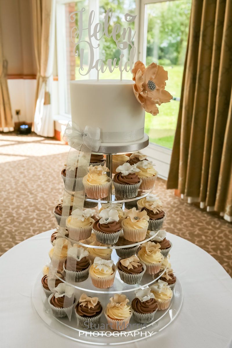 cup cakes sitting on a cake stand with a simple small wedding cake on the top