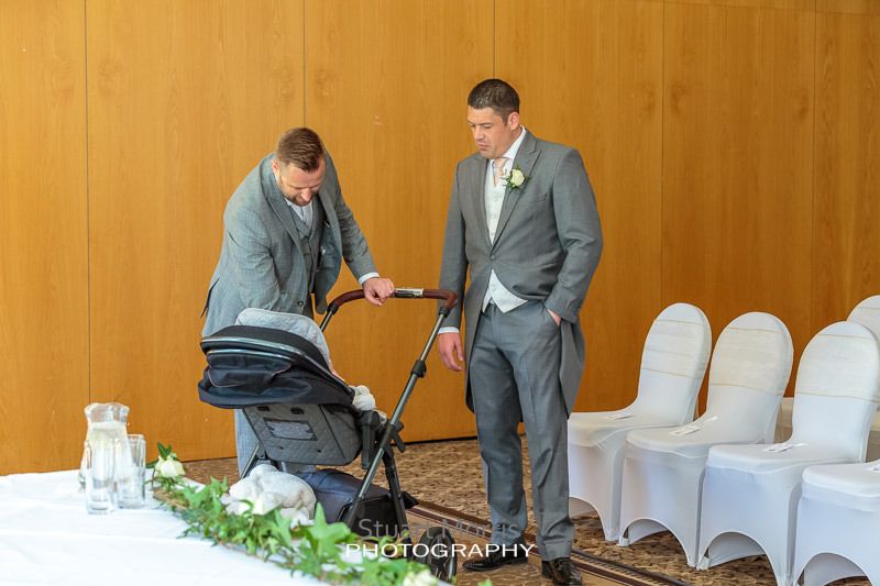 one of the groomsmen sees to his baby in the pram watched by another groomsman