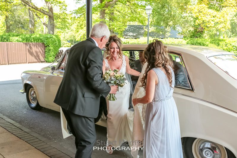 the bride climbs out of the wedding car helped by the chauffeur