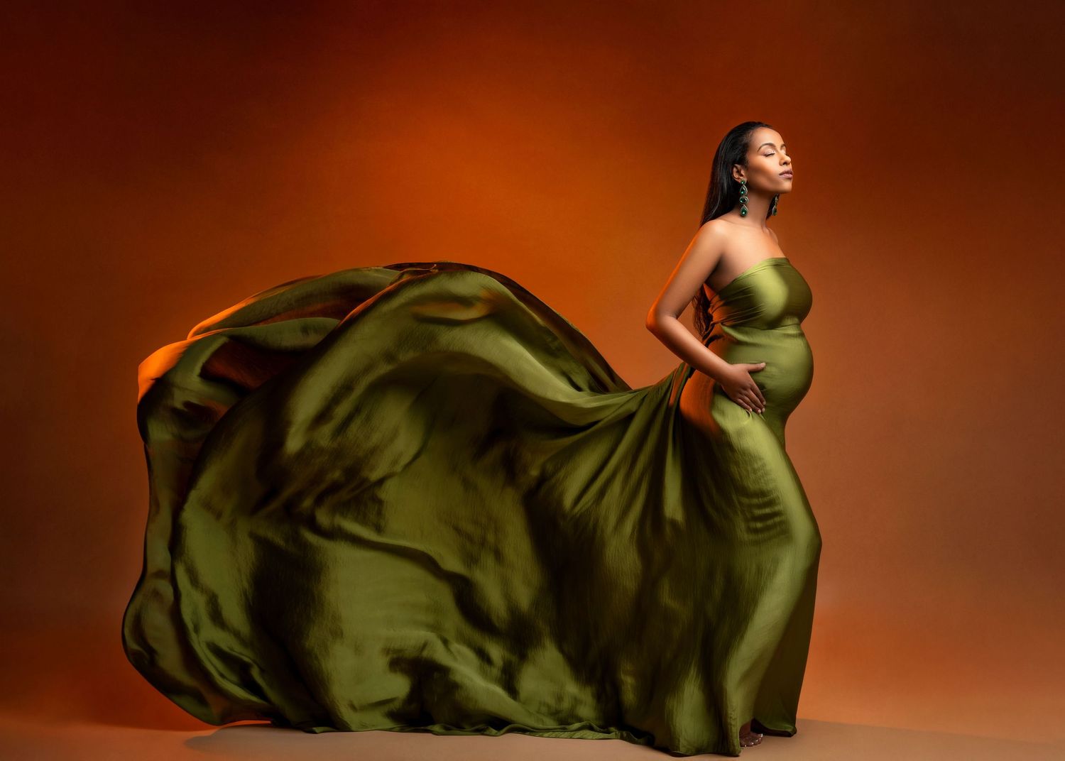 a pregnant woman stands in studio with her dress flowing behind her