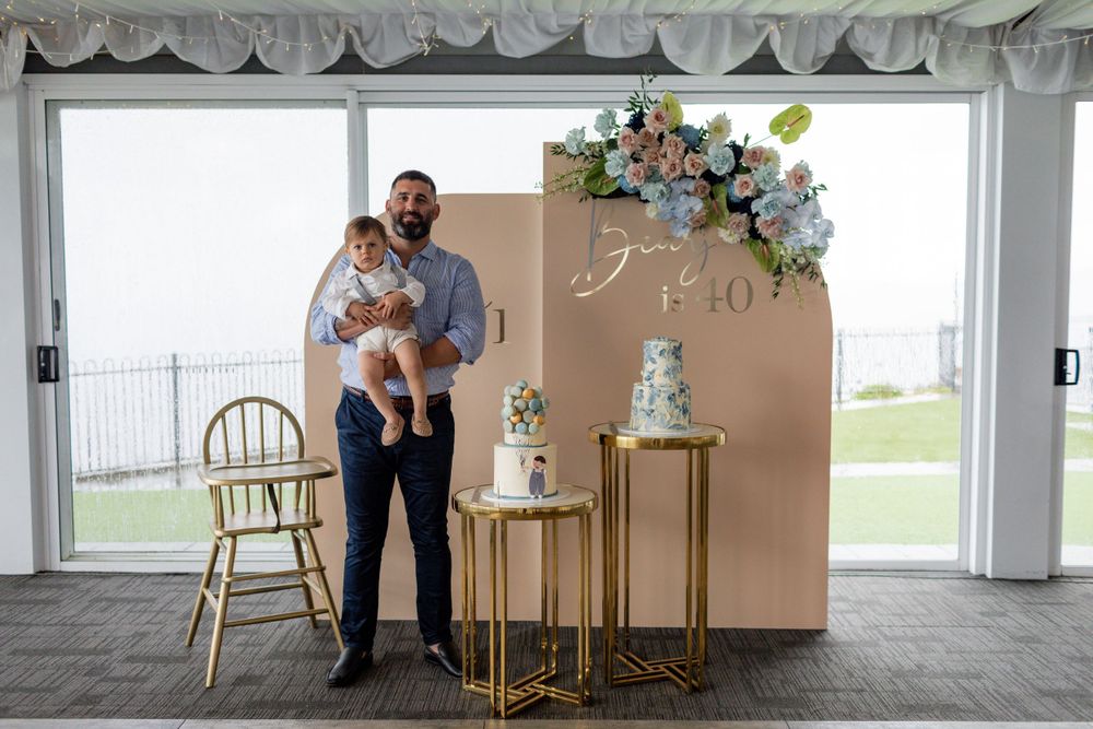 Elegant party display setup with beige backdrop, gold furniture and blue floral arrangements.