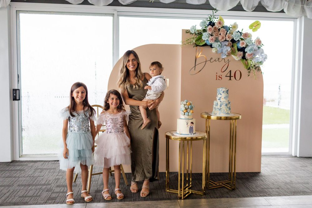 Family gathering in front of decorated backdrop with tiered cake display.