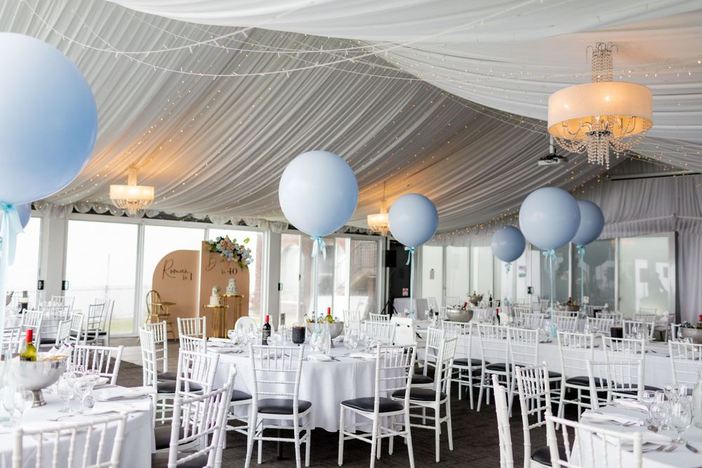 Elegant white reception room with draped ceiling, blue balloons and white chiavari chairs.