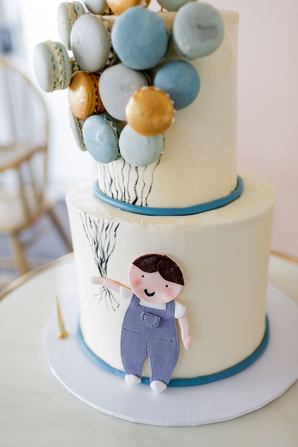 Close up of a whimsical cake with blue and gold macarons arranged as floating balloons.