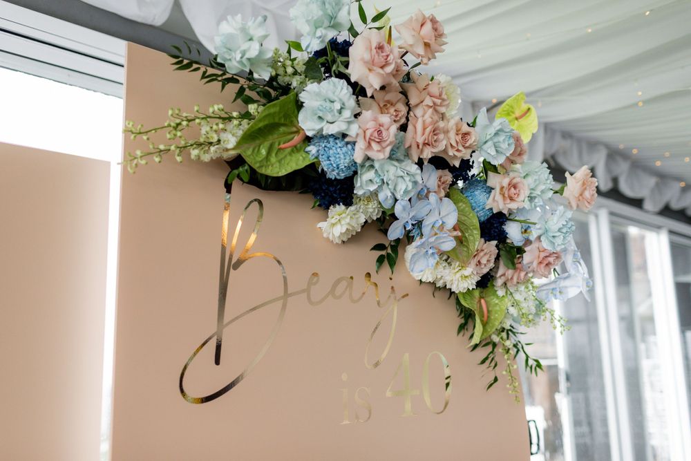 Elegant floral arrangement with blue and pink blooms adorning a beige wall with script lettering.